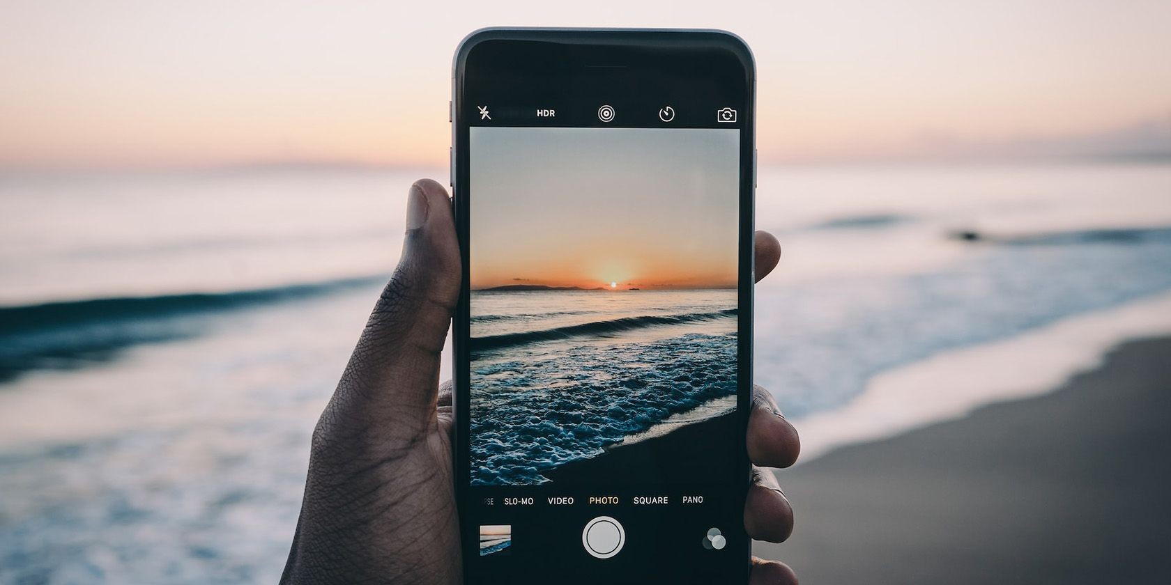 A hand holding an iPhone taking a picture of the ocean