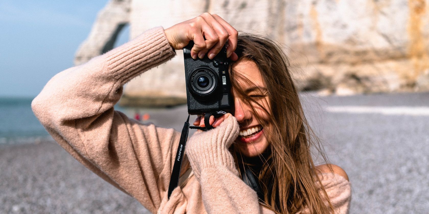 A woman holding a camera and taking photos of someone else with a cliff in the background