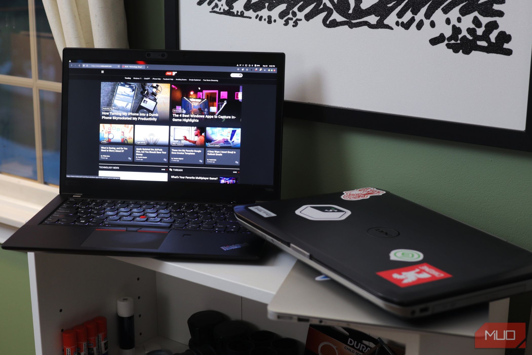 Hai laptop trên giá trắng với một máy được mở ra trang MakeUseOf.