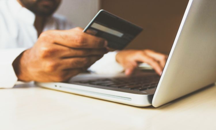 Một người đàn ông đang gõ phím trên laptop trong khi cầm và nhìn vào một thẻ tín dụng