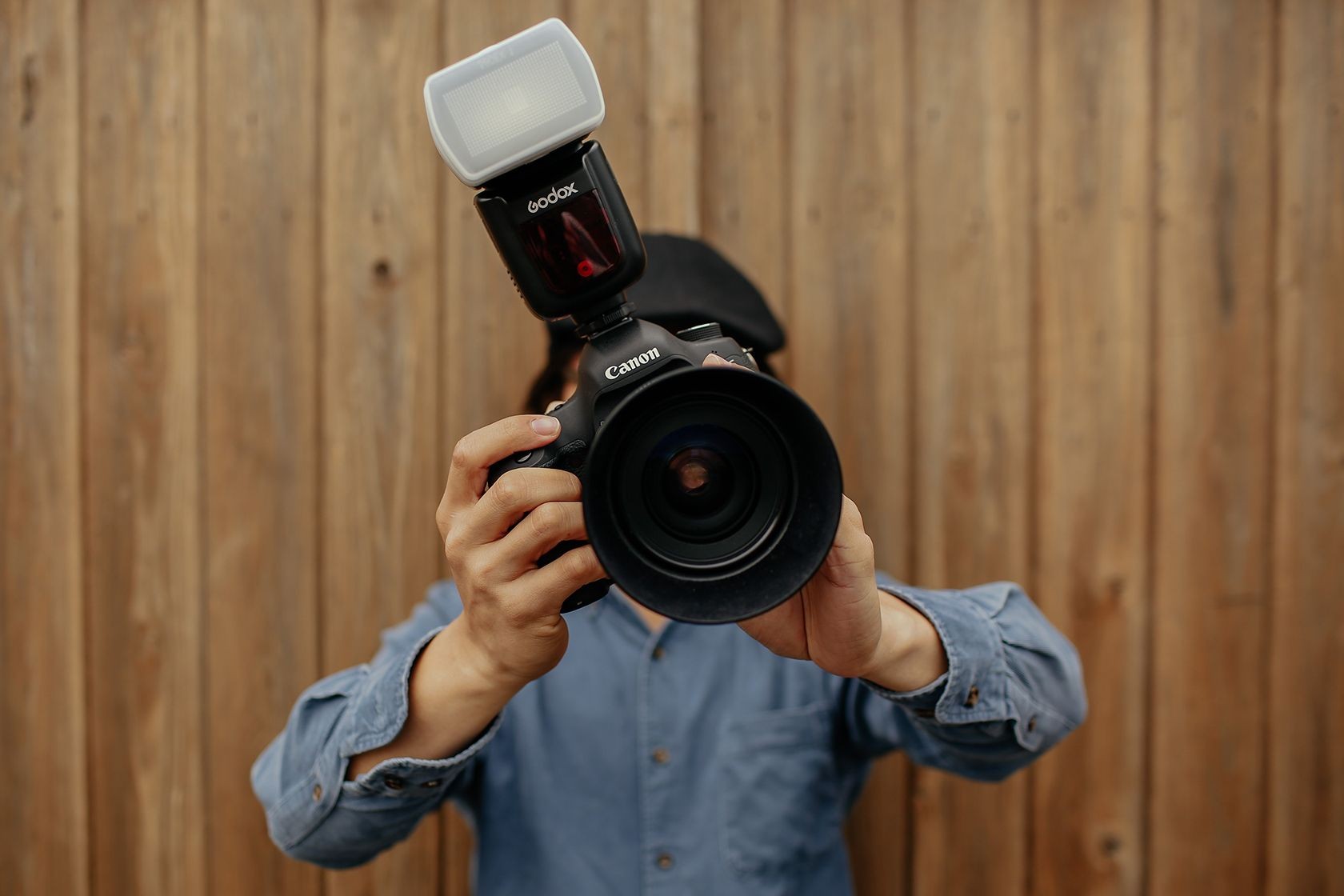 Người cầm máy ảnh Canon DSLR với ống kính góc rộng và đèn flash