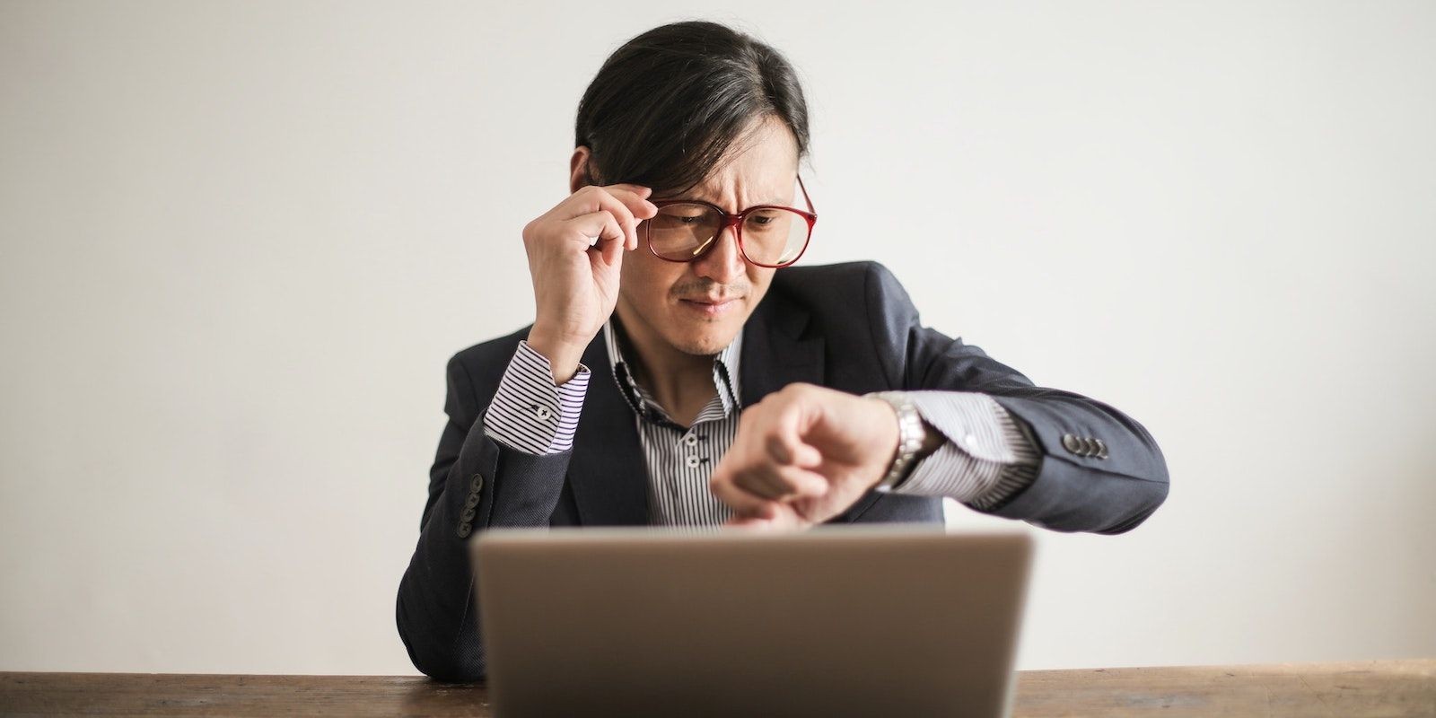 Người đàn ông bực bội kiểm tra đồng hồ trong khi sử dụng laptop