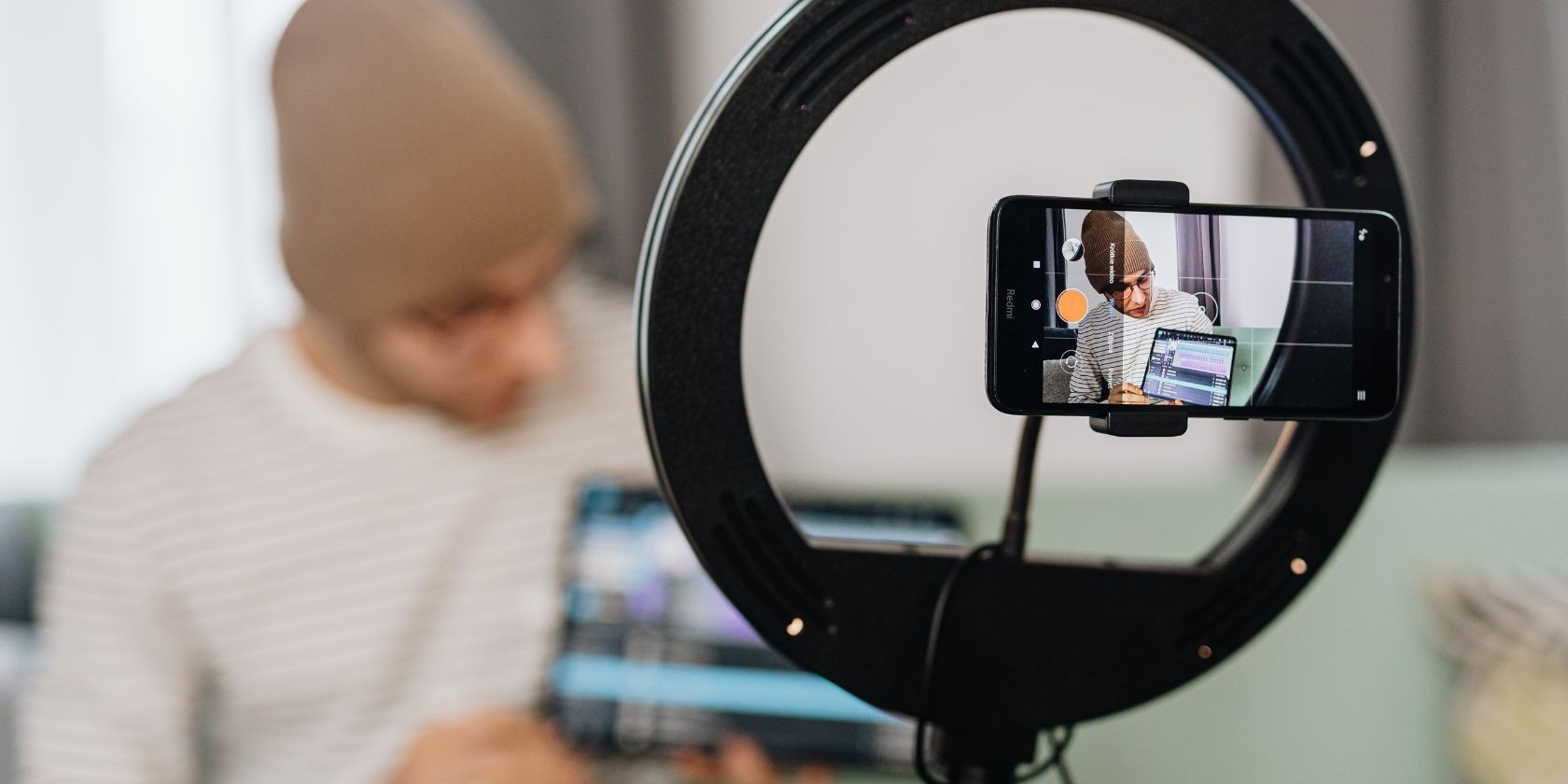 Người đàn ông đeo mũ len và cầm máy tính bảng đang tạo vlog sử dụng đèn vòng và điện thoại di động
