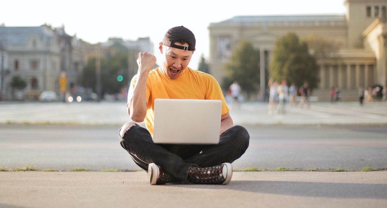 Người đàn ông vui mừng ngồi trên mặt đất với laptop bên ngoài