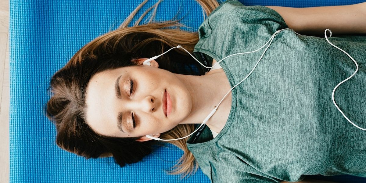 Người phụ nữ yên bình đeo tai nghe nghỉ ngơi trong tư thế Shavasana tại nhà