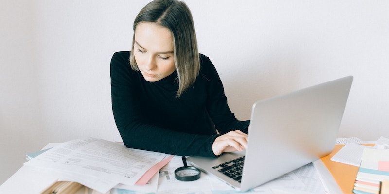 Phụ nữ làm việc giấy tờ trước máy tính xách tay