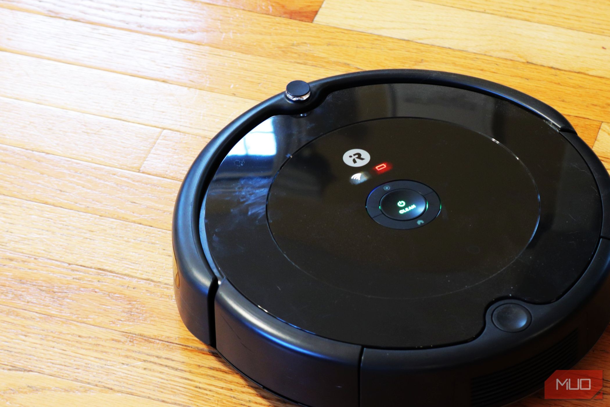 Robot hút bụi Roomba màu đen đối diện chéo trái trên sàn gỗ màu sáng